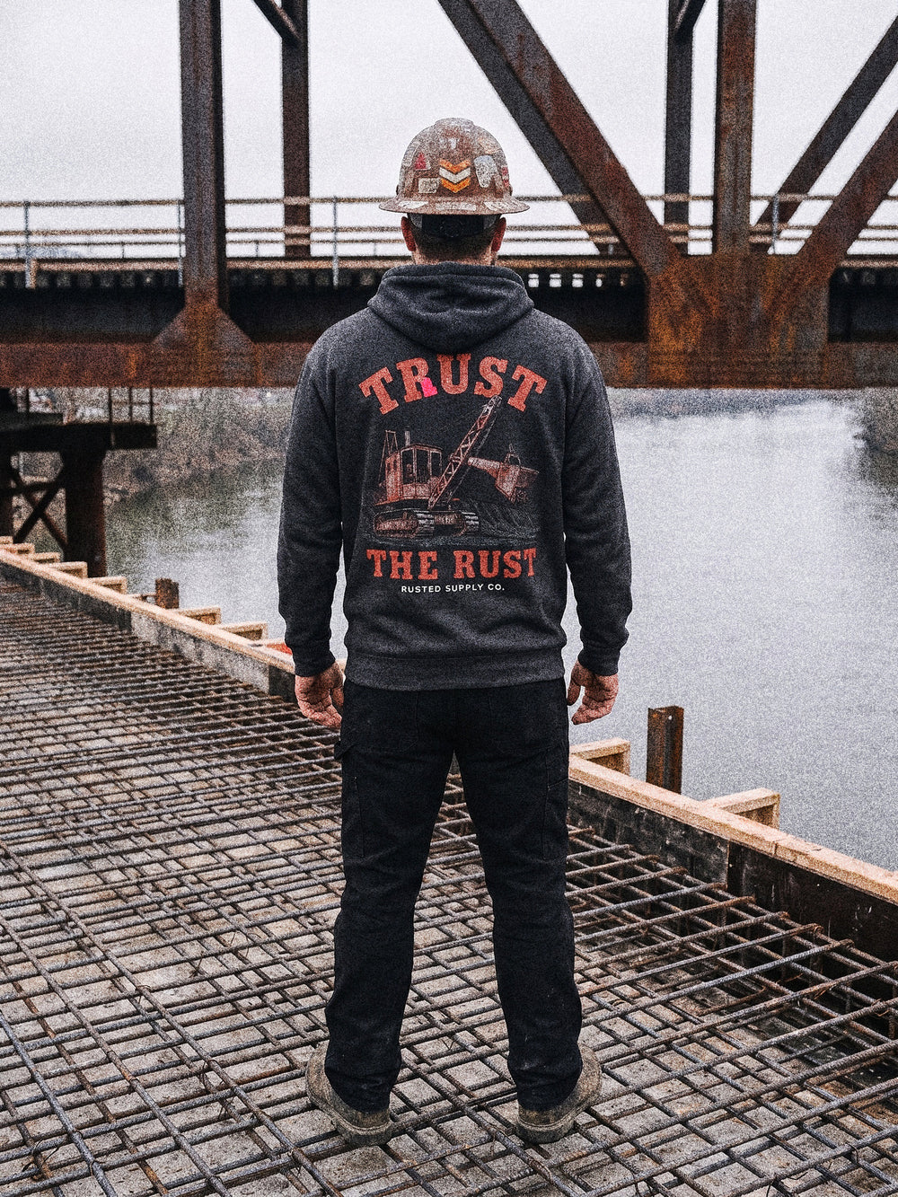 Tradesman in a TRUST THE RUST steam shovel hoodie on a bridge deck